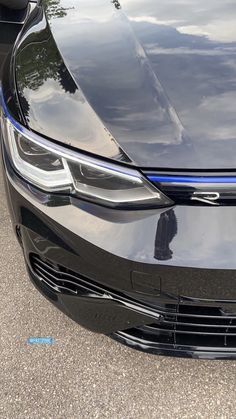 the front end of a black car parked in a parking lot next to another car