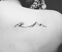 a black and white photo of a woman's back with mountains tattoo on it