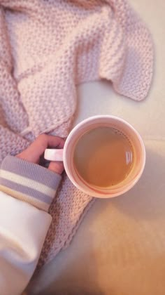 a person holding a cup of tea on top of a bed next to a blanket