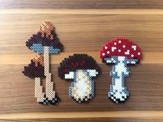 three pixellated mushrooms are sitting on a wooden surface, one is red and the other is blue