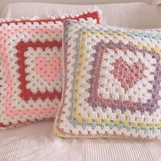 two crocheted pillows sitting on top of a white bed next to each other