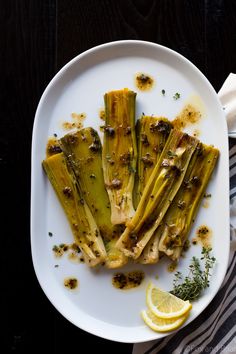 grilled artichokes on a white plate with lemon wedges and herbs