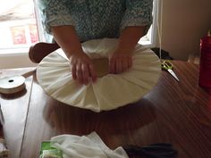 a woman is making a paper plate on a wooden table with other items around her