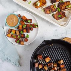 two plates with tofu on them next to a pan filled with other food items