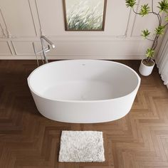 a large white bath tub sitting on top of a wooden floor next to a plant