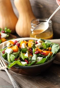 a person pouring dressing onto a salad in a bowl