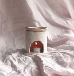 a white candle holder with a lit candle in it on a pink sheeted surface