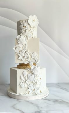 a three tiered wedding cake with white flowers on the side and gold accents, sitting on a marble surface