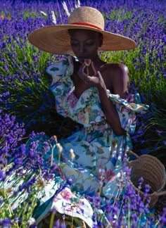 a woman sitting in a lavender field wearing a straw hat and holding a piece of fruit