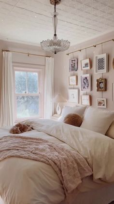 a white bed sitting under a window next to a lamp and pictures on the wall