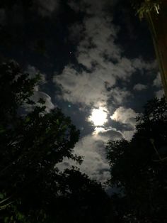 the moon shines brightly through the clouds in the night sky above some trees and bushes