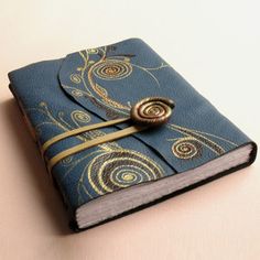 a blue notebook with an intricate design on the front and gold ribbon around the cover