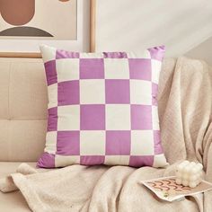 a purple and white checkered pillow sitting on top of a couch next to a remote control