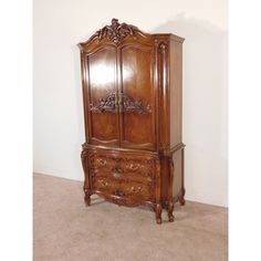 an antique wooden armoire with carvings on the top and bottom, sitting against a wall