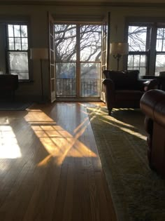 the sun shines through two large windows into a living room with hardwood floors and leather furniture