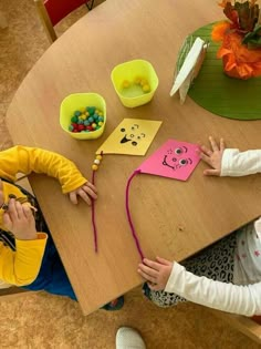 two young children sitting at a table with paper cutouts on it and beads in their hands