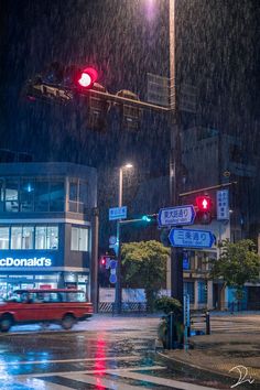 a red car driving down a street next to traffic lights in the rain at night