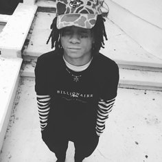 a young man with dreadlocks and a hat on his head is standing in front of some stairs