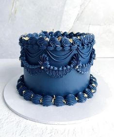 there is a blue cake with gold decorations on the top and bottom, sitting on a white plate