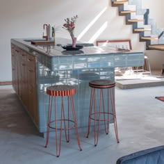 two stools are in front of an island with flowers on it and stairs leading up to the second floor