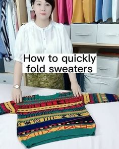 a woman standing next to a pile of sweaters on top of a white bed