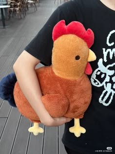 a person holding a stuffed animal chicken in their hands and wearing a black t - shirt