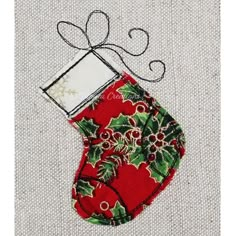 an embroidered christmas stocking with holly and bells on the side, in a green frame