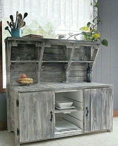 an old wooden hutch with dishes and utensils on it in front of a window