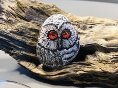 an owl rock sitting on top of a piece of driftwood with eyes painted red