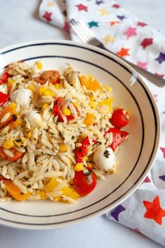 a white plate topped with pasta and veggies on top of a table next to a fork