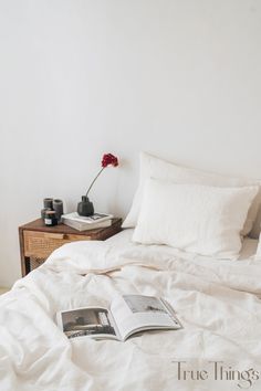 a bed with white linens and two books on the end table next to it