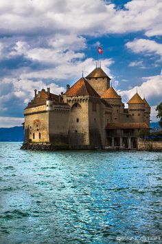 an old castle sitting on top of a lake next to a shore with blue water