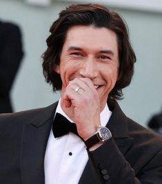 a man in a tuxedo is smiling and holding his hand to his mouth