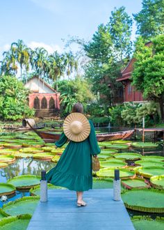 a woman in a green dress is standing on a dock and looking at lily pads