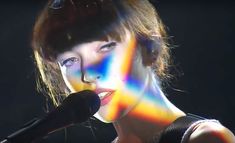 a woman that is standing in front of a microphone with colored paint on her face