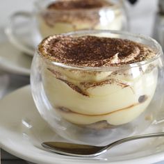 two desserts in glass bowls with spoons on a plate next to each other