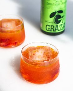 two glasses filled with liquid sitting next to a can of grape soda on a table