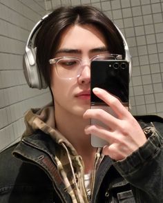 a young man wearing headphones and looking at his cell phone in the bathroom while listening to music