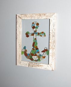 an anchor made out of sea glass in a white frame