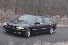 a black bmw parked in front of some trees