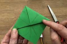 someone is cutting out an origami leaf from green paper with scissors on the table