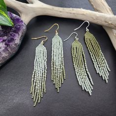 three pairs of beaded earrings sitting on top of a table next to a branch