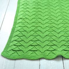 a green knitted blanket sitting on top of a white wooden floor next to a cup