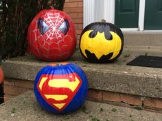 three pumpkins painted to look like batman and superman logos are sitting on the steps