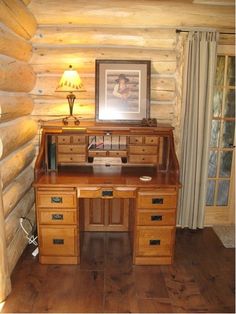 a wooden desk sitting in the corner of a room next to a lamp and window