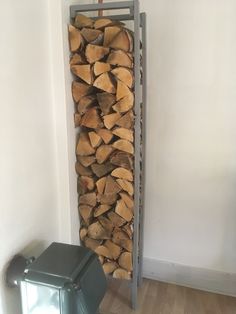 a stack of firewood sitting next to a trash can in a room with white walls