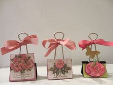 three small boxes with pink flowers and ribbons on them, one is holding a heart