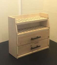 a wooden cabinet with two drawers sitting on top of a black floor next to a white wall