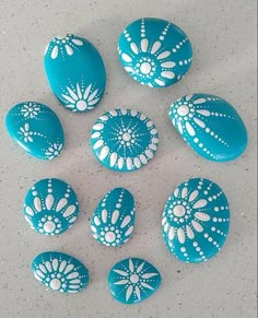 six blue and white painted rocks on a counter top with holes in the middle to show designs