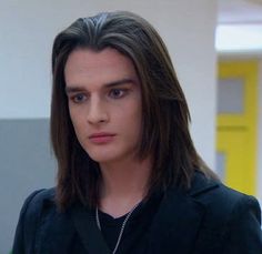 a young man with long hair wearing a black shirt and looking off to the side